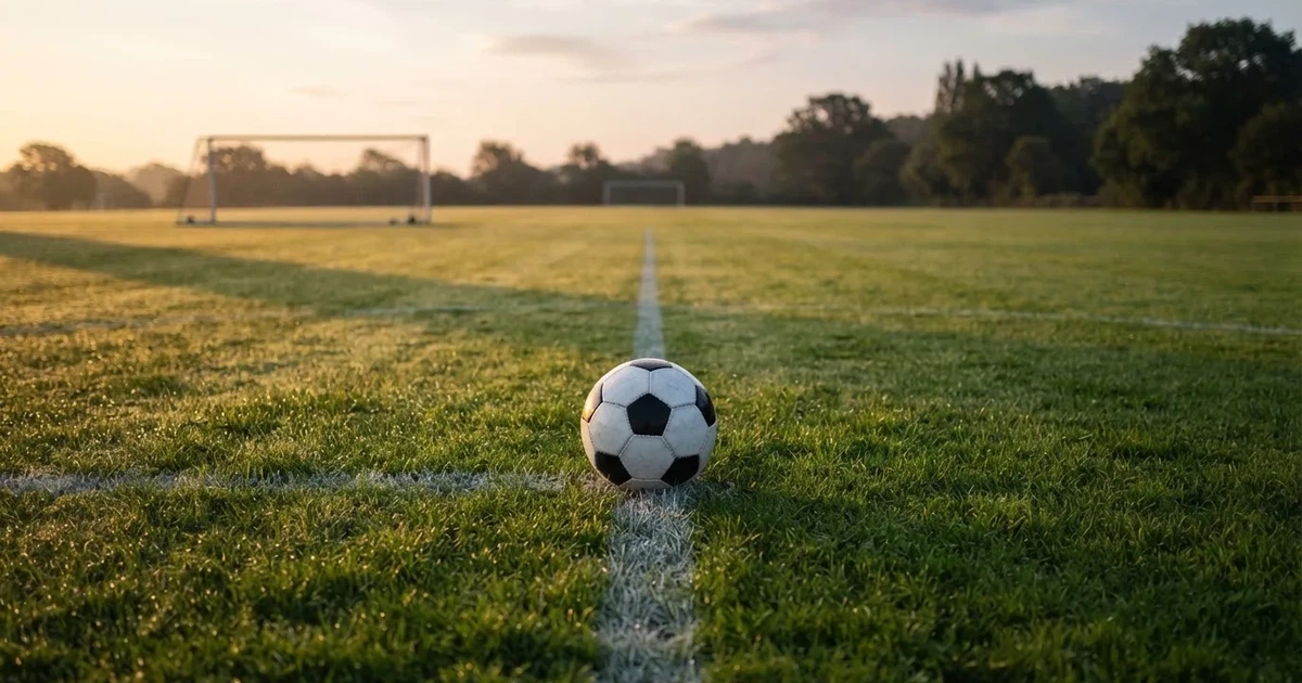 Een voetbal op de middenstip van een grasveld in het ochtendlicht
