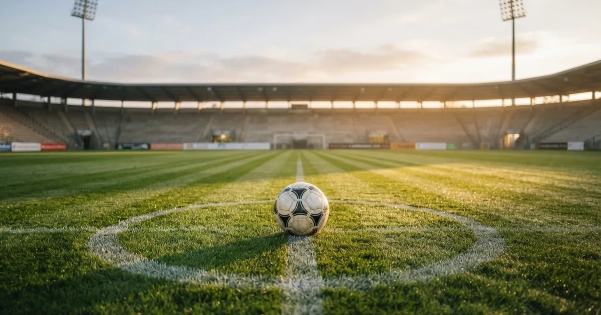 Een voetbal op de middenstip van een grasveld in het ochtendlicht