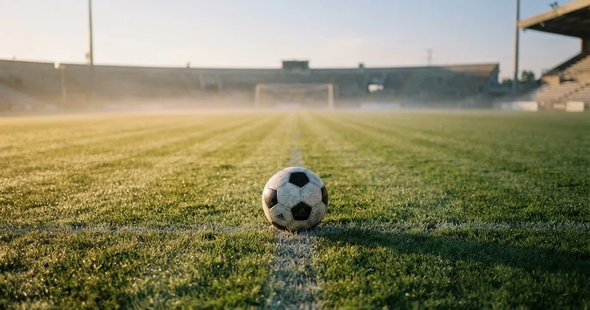 Een voetbal op de middenstip van een grasveld in het ochtendlicht