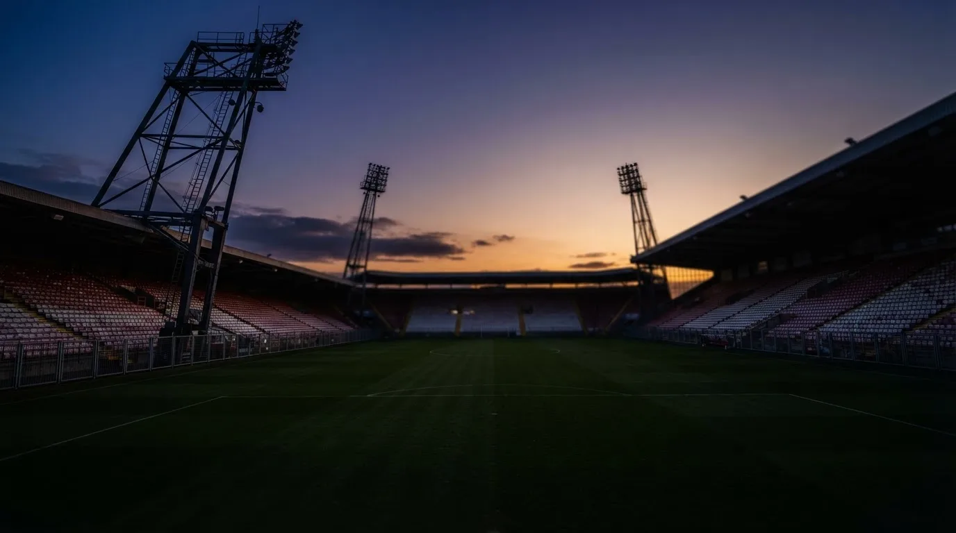 Een leeg voetbalstadion met lichtmasten bij schemering