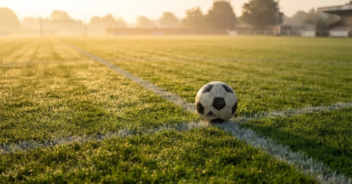 Een voetbal op de middenstip van een grasveld in het ochtendlicht