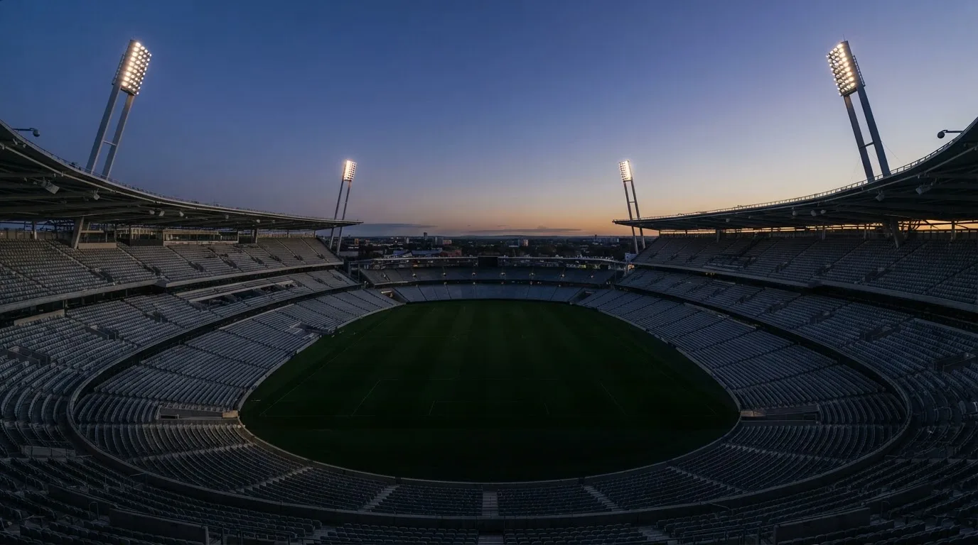 Een leeg voetbalstadion met lichtmasten bij schemering