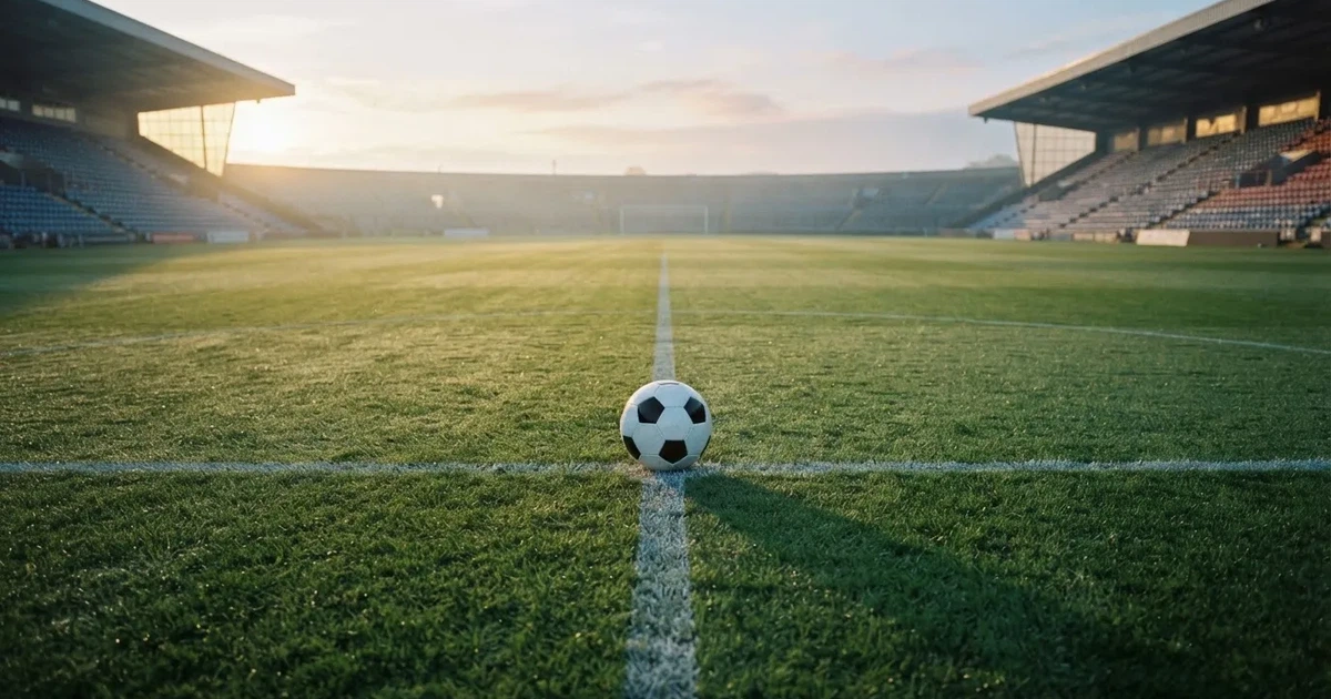 Een voetbal op de middenstip van een grasveld in het ochtendlicht